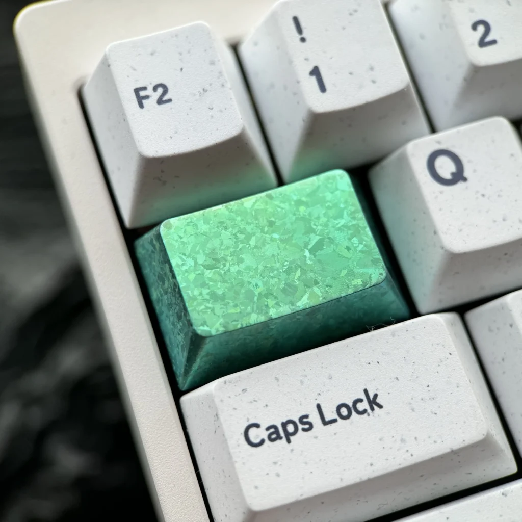 Close-up of a premium Ice Crystal Titanium Keycap, showcasing its shimmering, jewel-like facets and vibrant metallic color.