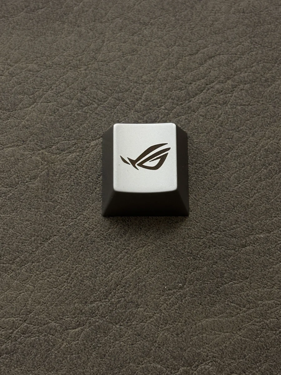 Close-up views of the ROG Logo Alloy Keycaps, showcasing its aggressive angular design in a premium metallic finish from various angles.