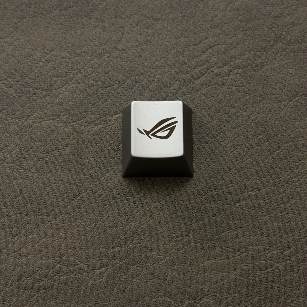 A single, exclusive silver ROG Logo Alloy Keycaps, meticulously crafted with an aggressive, angular design for magnetic switches, embodying powerful stye.