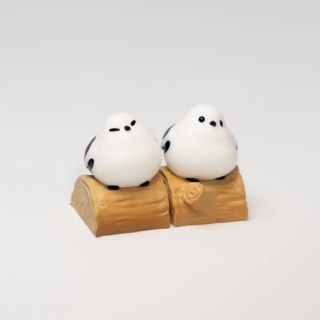 A charming handcrafted whimsical Bushtit artisan keycap, showcasing the adorable 3D sculpted forest bird playfully perched on its rustic log from an engagement.