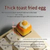 Close-up views of the whimsical handcrafted 3D fried egg toast artisan keycap, showcasing its vibrant yellow and white details from multiple angles.