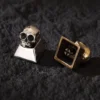 Two skull keycaps, one brass and one cupronickel, side-by-side on a dark surface.