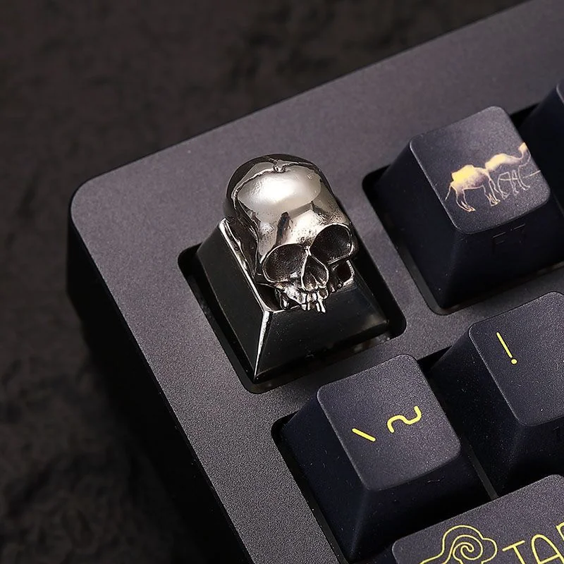 A brass skull keycap mounted on an ESC key position, integrating with a dark themed keyboard.